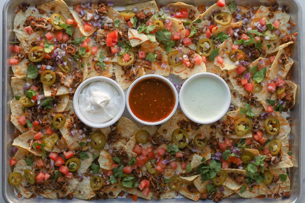 Baked nacho with ground beef, cheese, toppings and dip on tray.