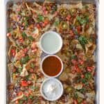 Nachos with toppings and dip on a baking sheet.