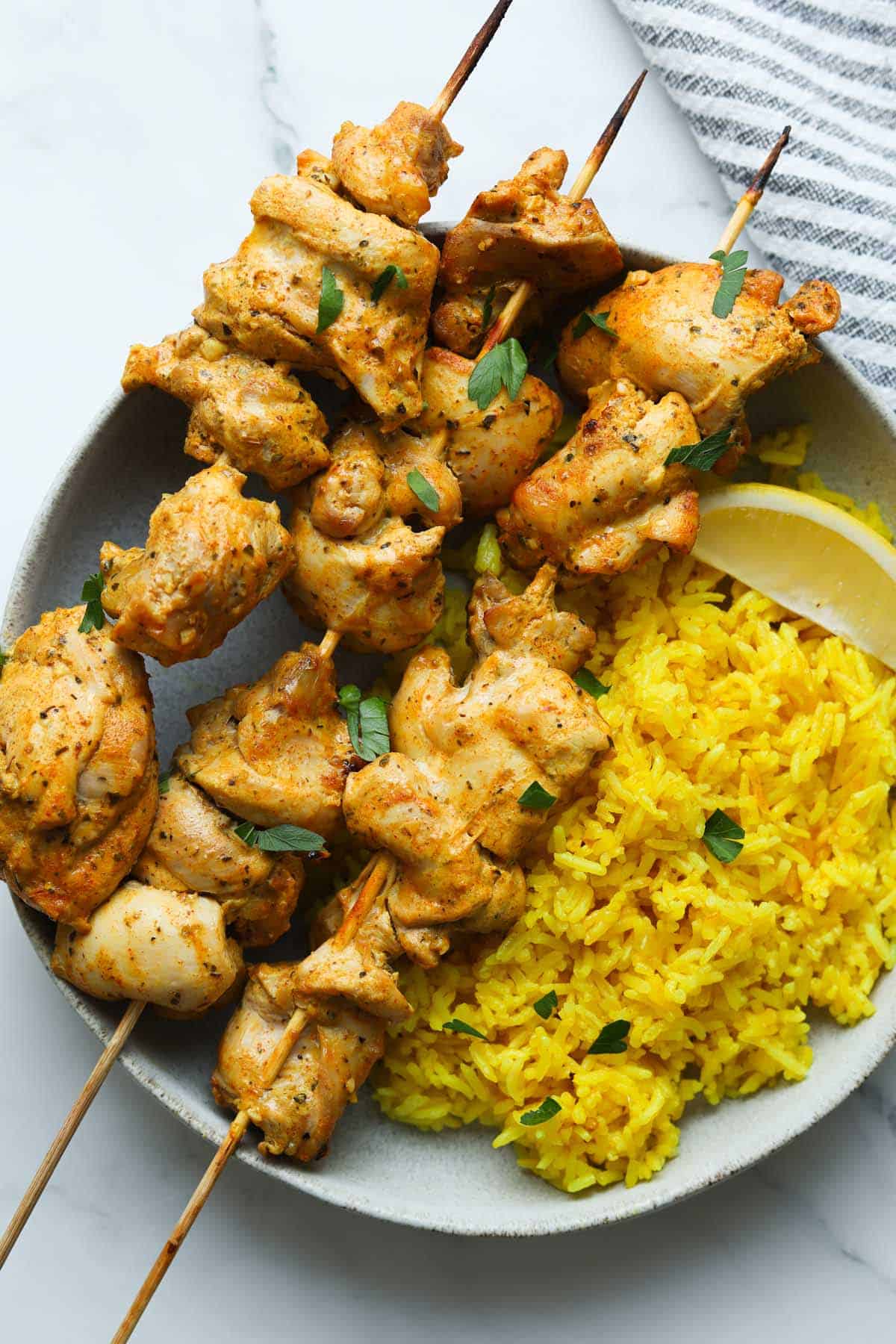 Chicken skewers with yellow rice on plate.