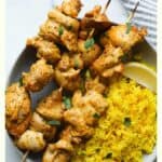 Chicken skewers with yellow rice on plate.