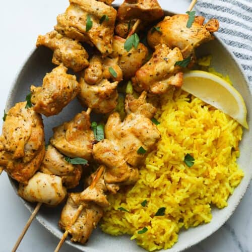 chicken skewers with yellow rice on plate.