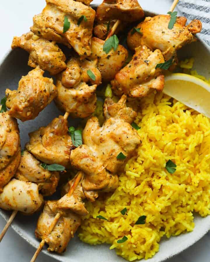 chicken skewers with yellow rice on plate.