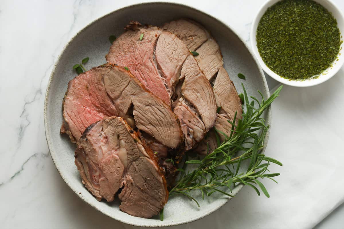 Sliced roasted lamb on plate with side of mint sauce.