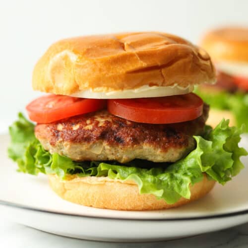 Hamburger with tomatoes, and lettuce on plate.