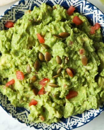 Bowl of guacamole with pepitas and diced tomatoes.