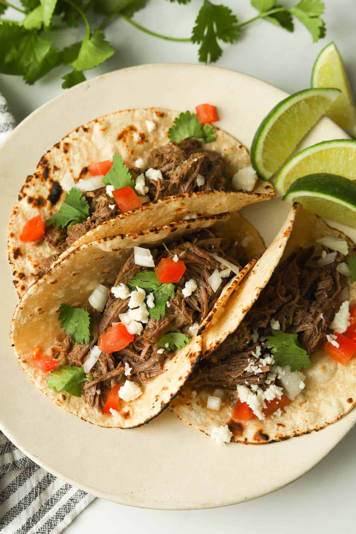 Shredded beef tacos garnished with cheese, onions, cilantro and tomatoes.