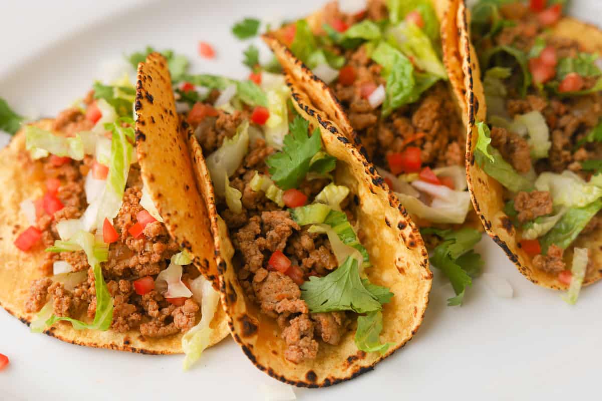 Ground meat tacos garnished with lettuce, cilantro and tomtoes.