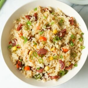 Bowl of fried rice with sausage, vegetables, eggs and green onions.