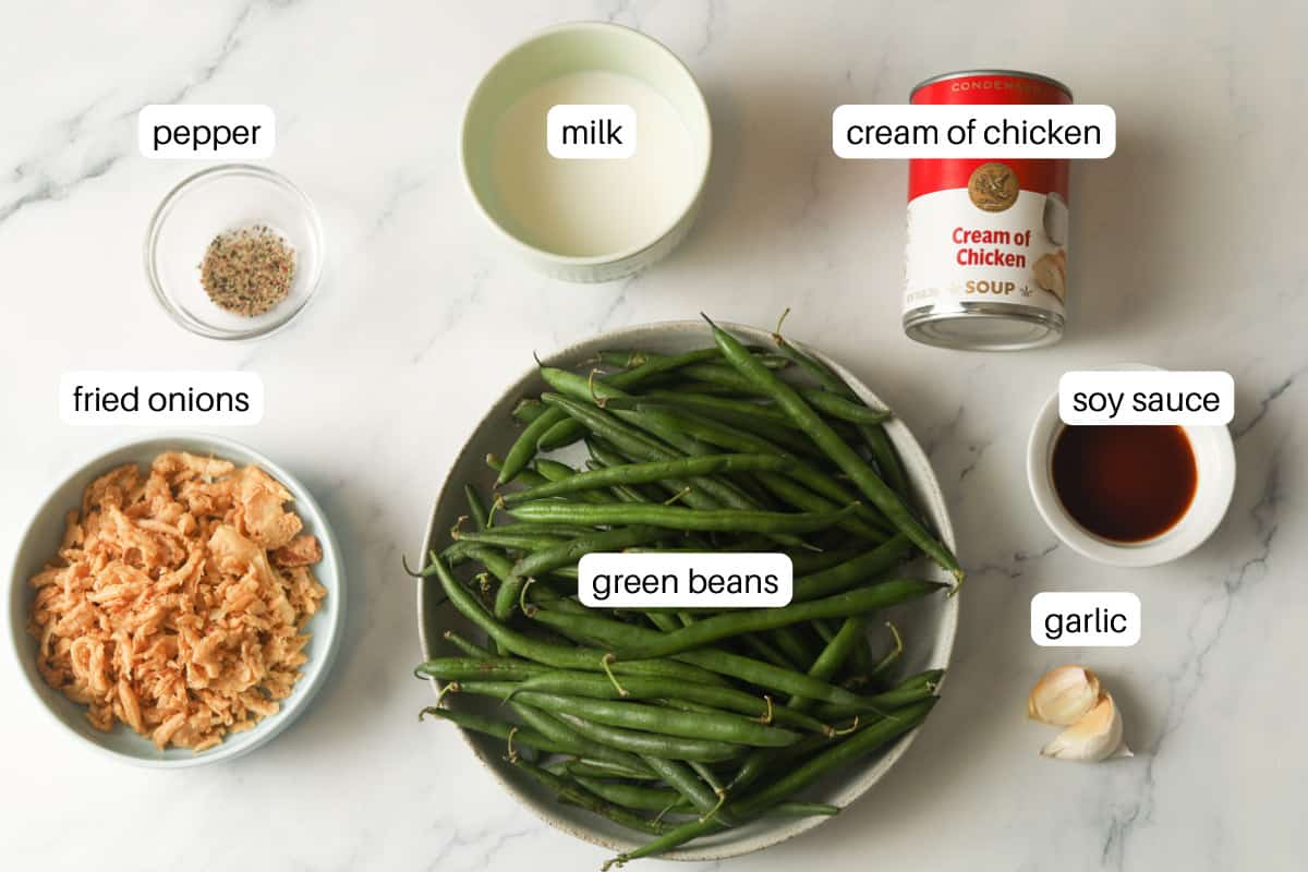Green beans, pepper, fried onions, milk, cream of chicken soup, soy sauce and garlic on table.