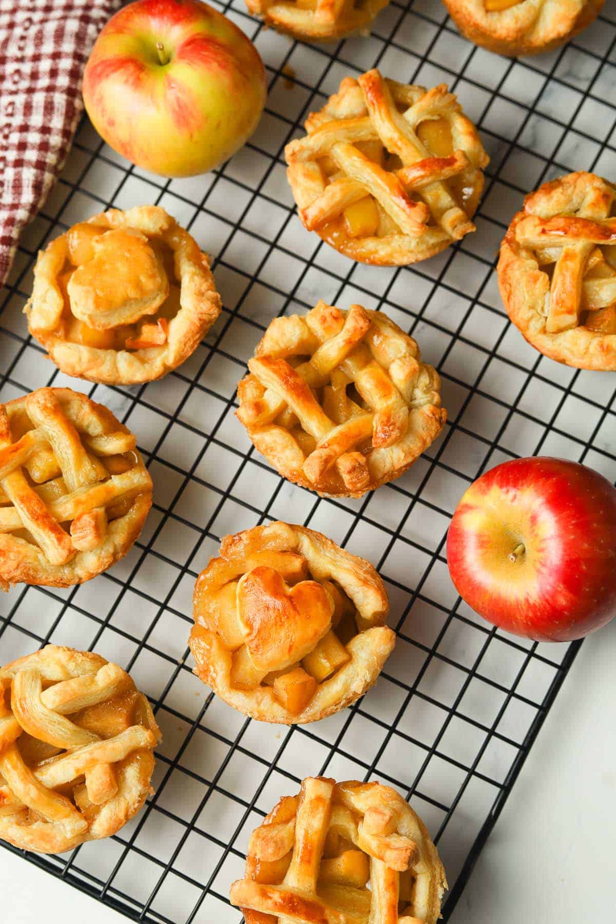 Mini apple pies and red apples on cooling rack.