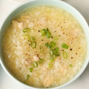 Rice congee with chicken bits garnished with sliced scallions and cracked pepper.