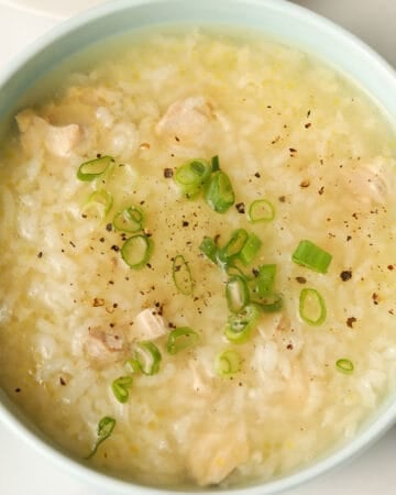 Rice congee with chicken bits garnished with sliced scallions and cracked pepper.