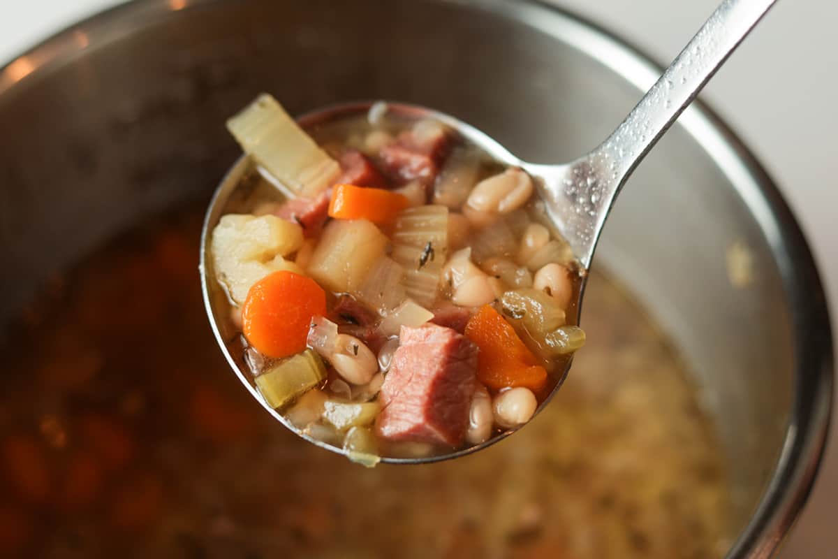 Ladle with a scoop white bean, diced ham, potatoes, carrots and celery soup.