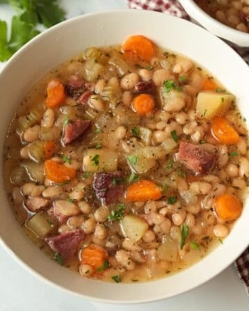 Bowl with white beans, diced ham, carrots and potato soup, garnished with parsley.