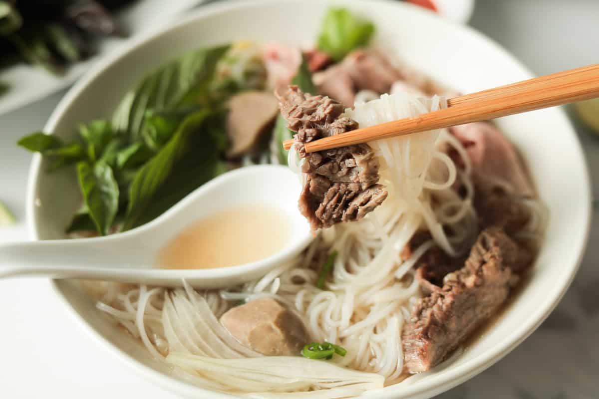 chopsticks holding a piece of meat over a bowl or rice noodle beef soup.