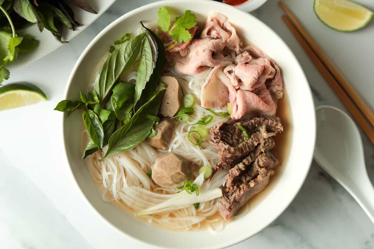 Bowl of rice noodle beef soup with herb garnish.