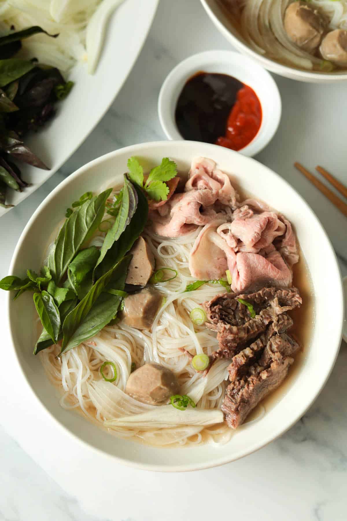 Bowl of rice noodle beef soup with herb garnish.