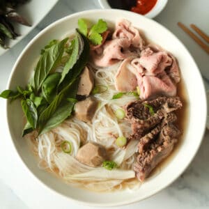 Bowl of rice noodle beef soup with herb garnish.