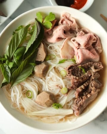 Bowl of rice noodle beef soup with herb garnish.