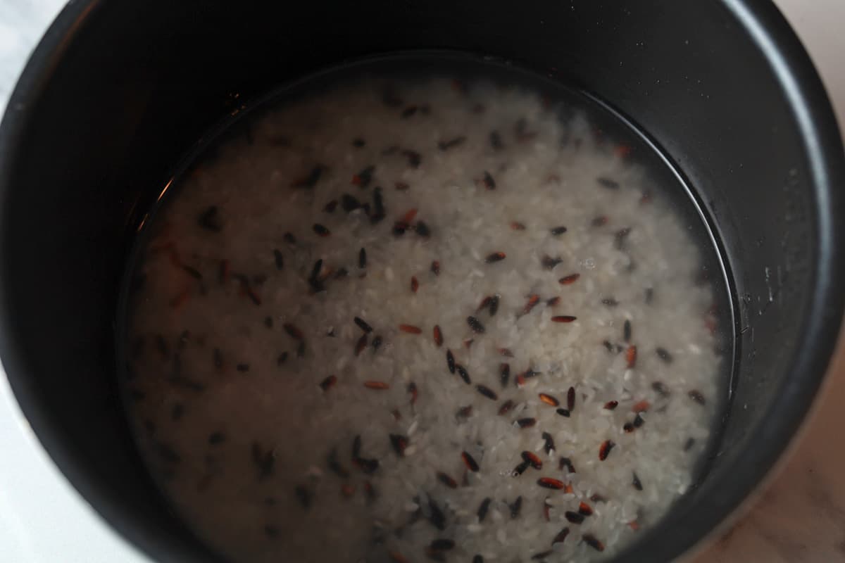 uncooked short grain and black rice in a rice cooker pot with water.