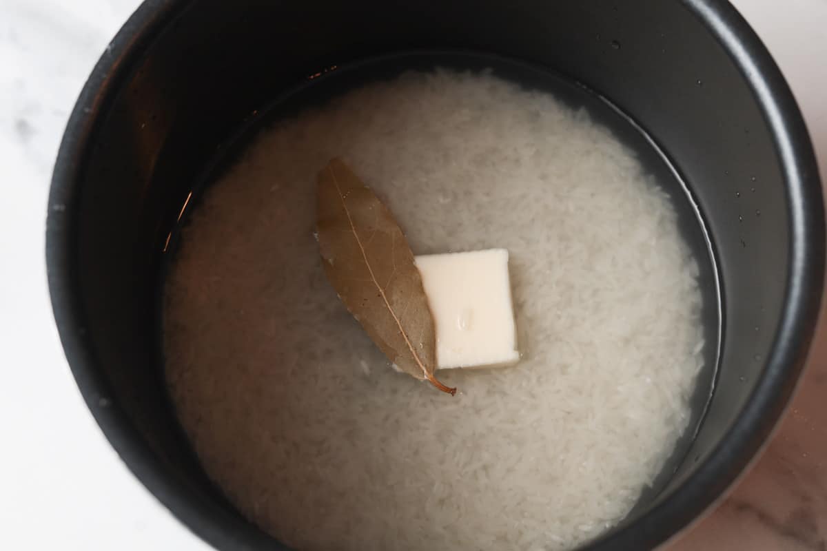 Rice in rice pot with butter and bay leaf.