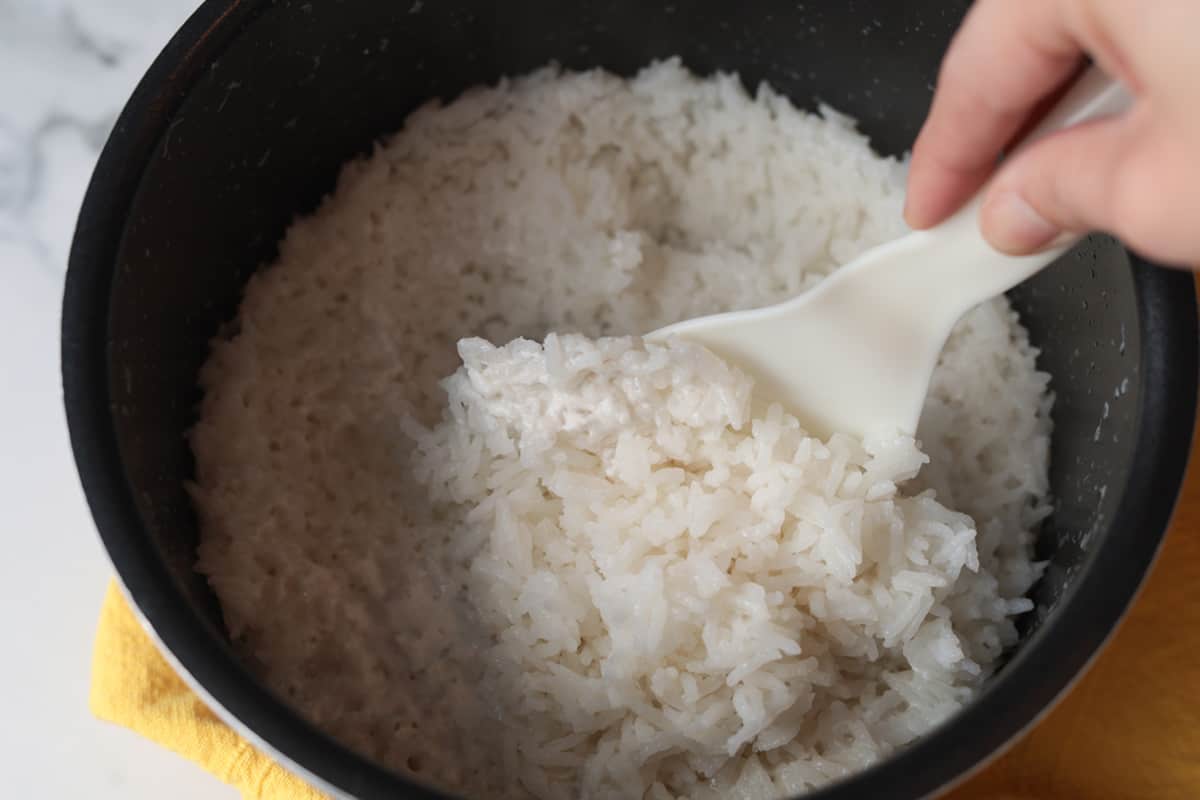 Spoon fluffing rice in rice cooker.