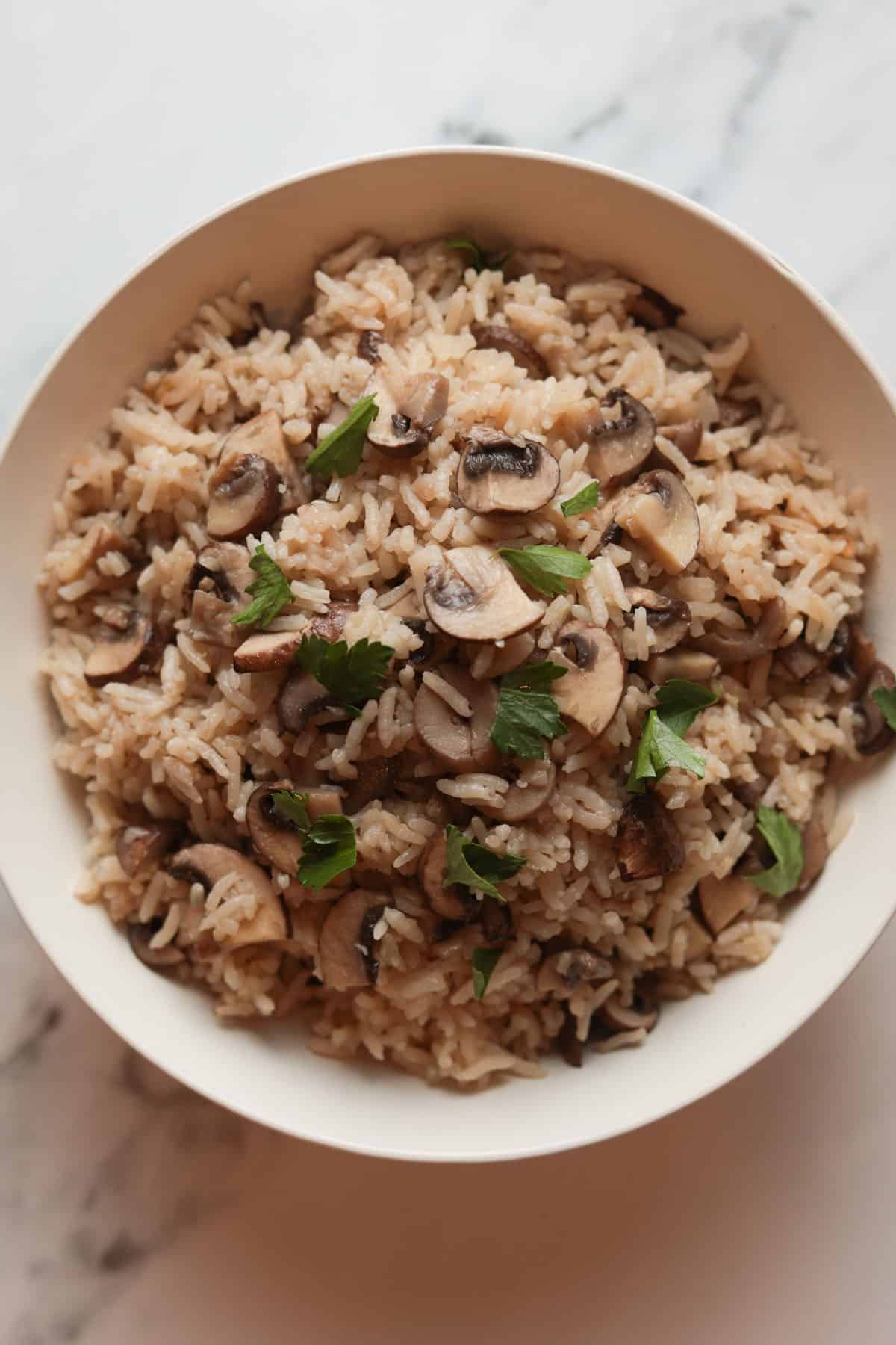Bowl of white rice with sliced mushrooms, garnished with parsley.