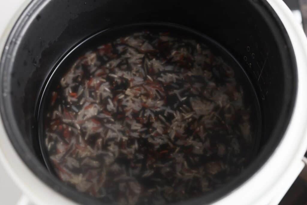 Wild rice in rice cooker pot with water.