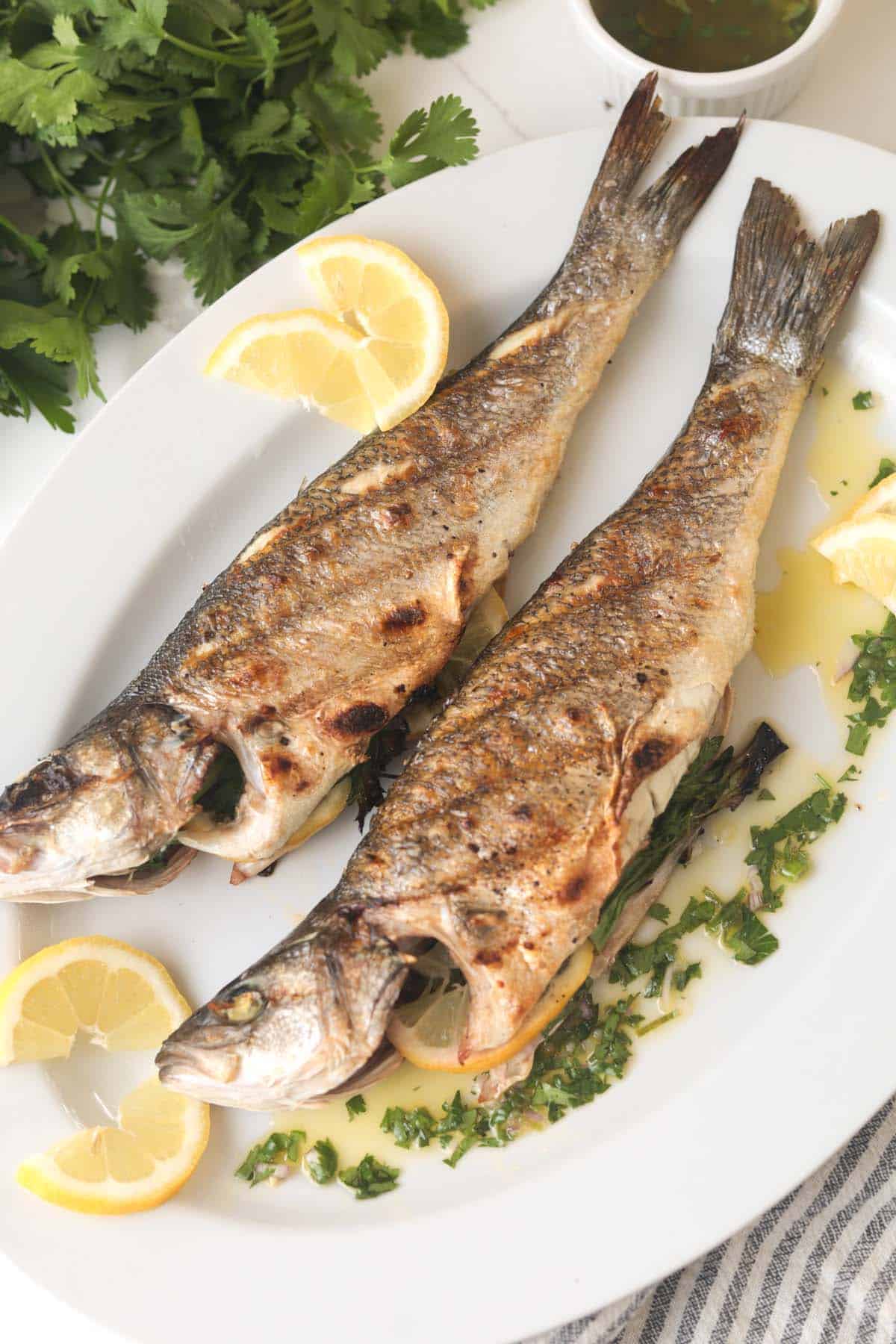 Two whole grilled branzino with lemon slices and herb sauce.