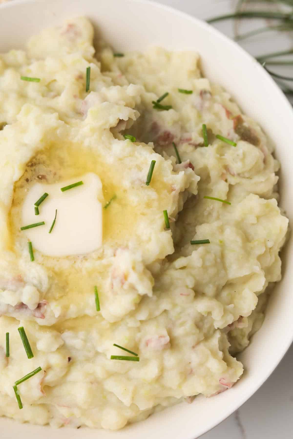 Closeup of garlic red mashed potatoes with skin, topped with butter and chives