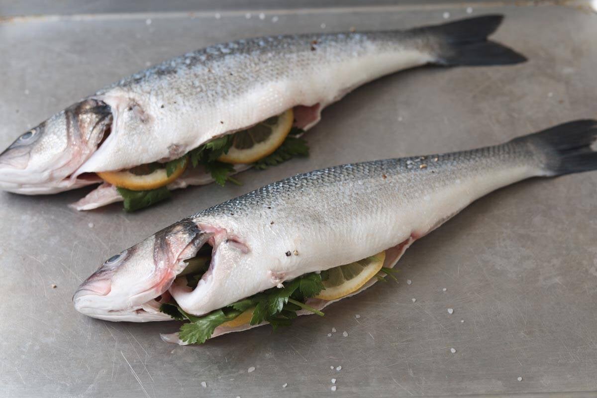 Two whole raw branzino stuffed with herbs and lemon.