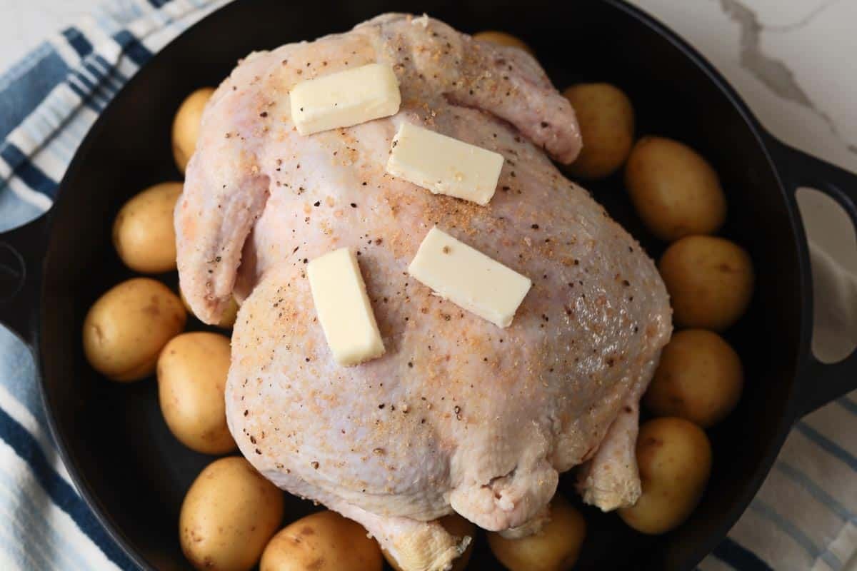 Raw whole chicken and potatoes in cast iron