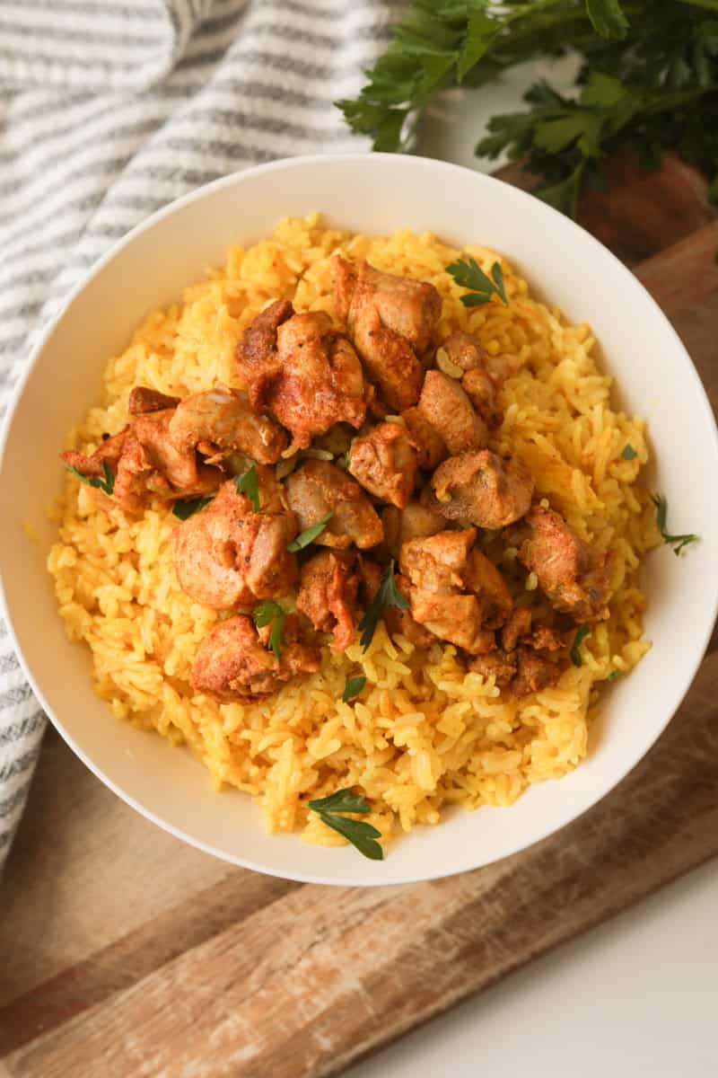 yellow rice topped with chicken pieces in bowl.