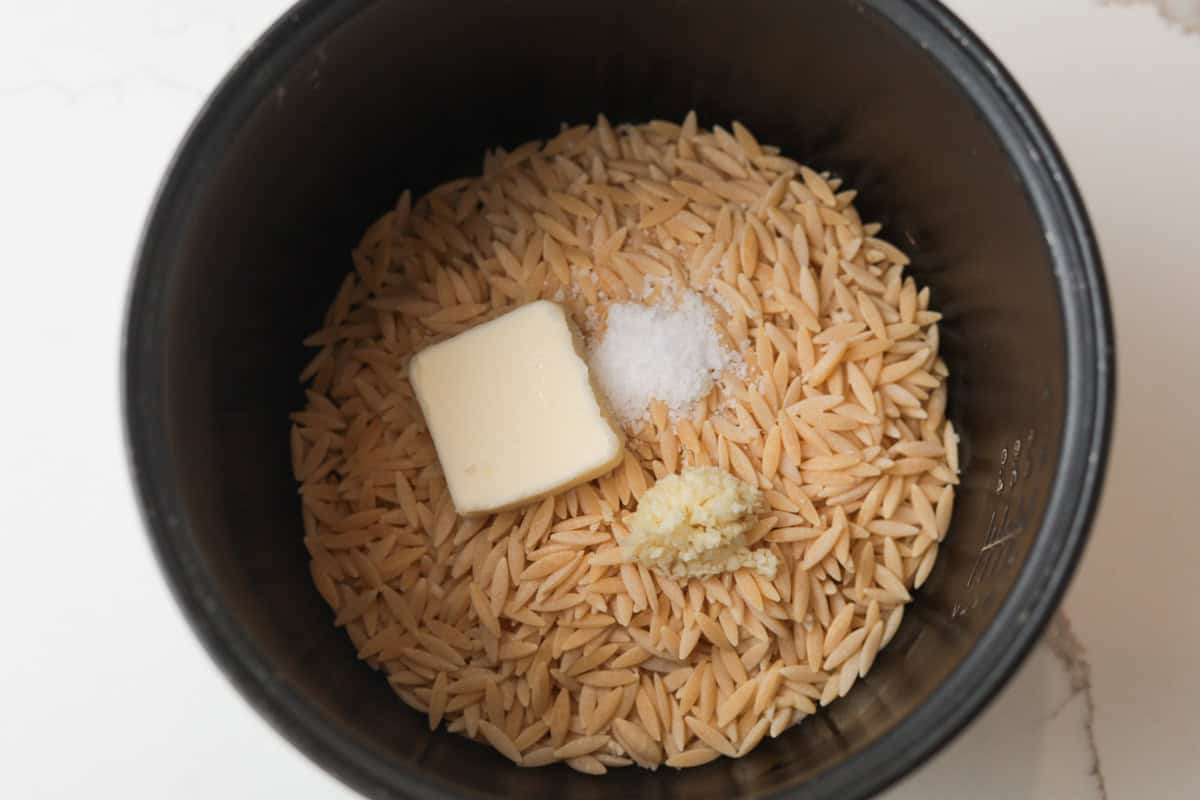 Uncooked orzo, butter, salt and garlic in rice cooker pot.