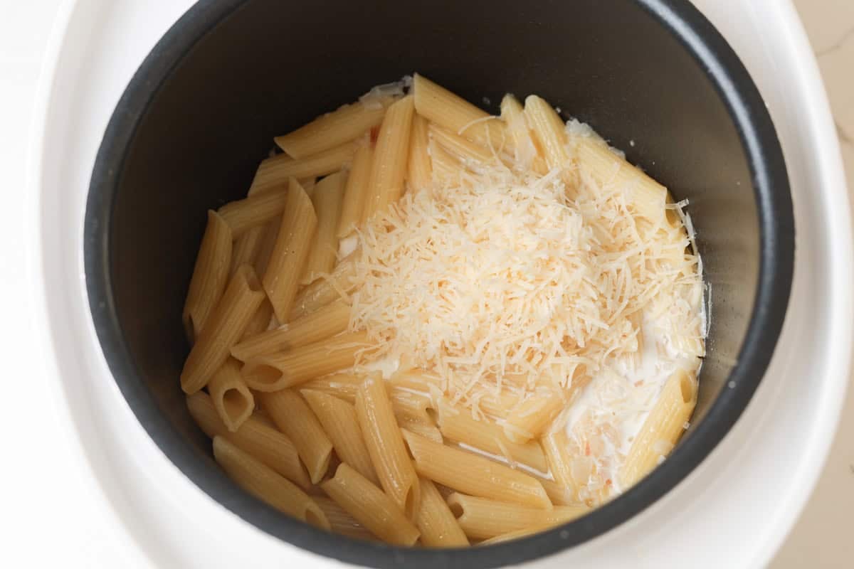 Cheese and cooked penne pasta in rice cooker pot.