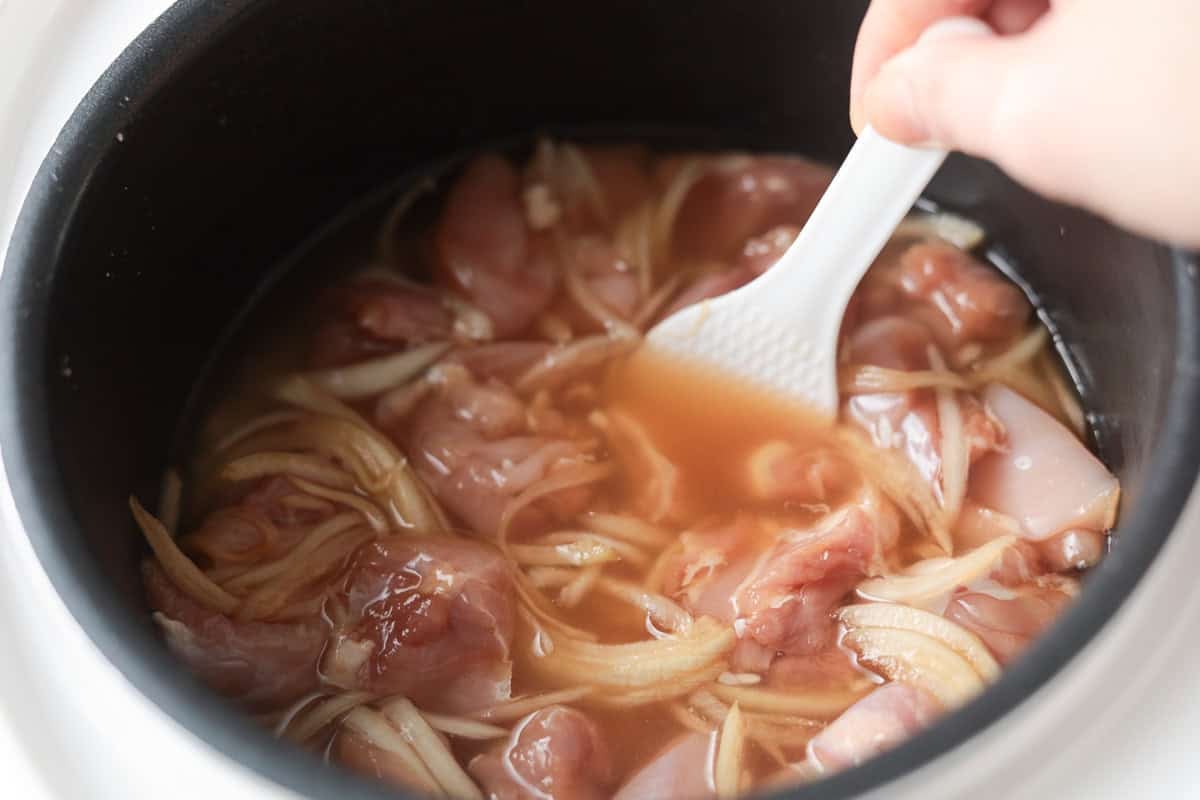 Onion, chicken and rice in rice cooker pot.