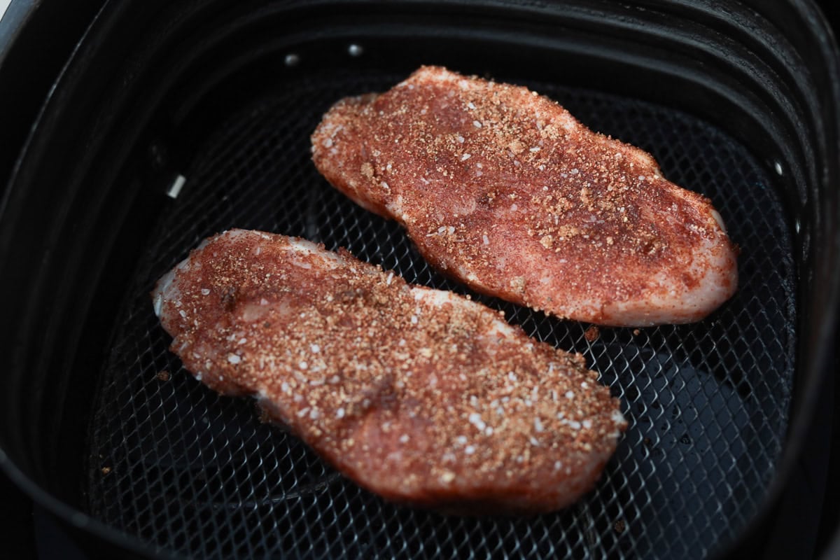 Two boneless pork loin chops in air fryer basket.