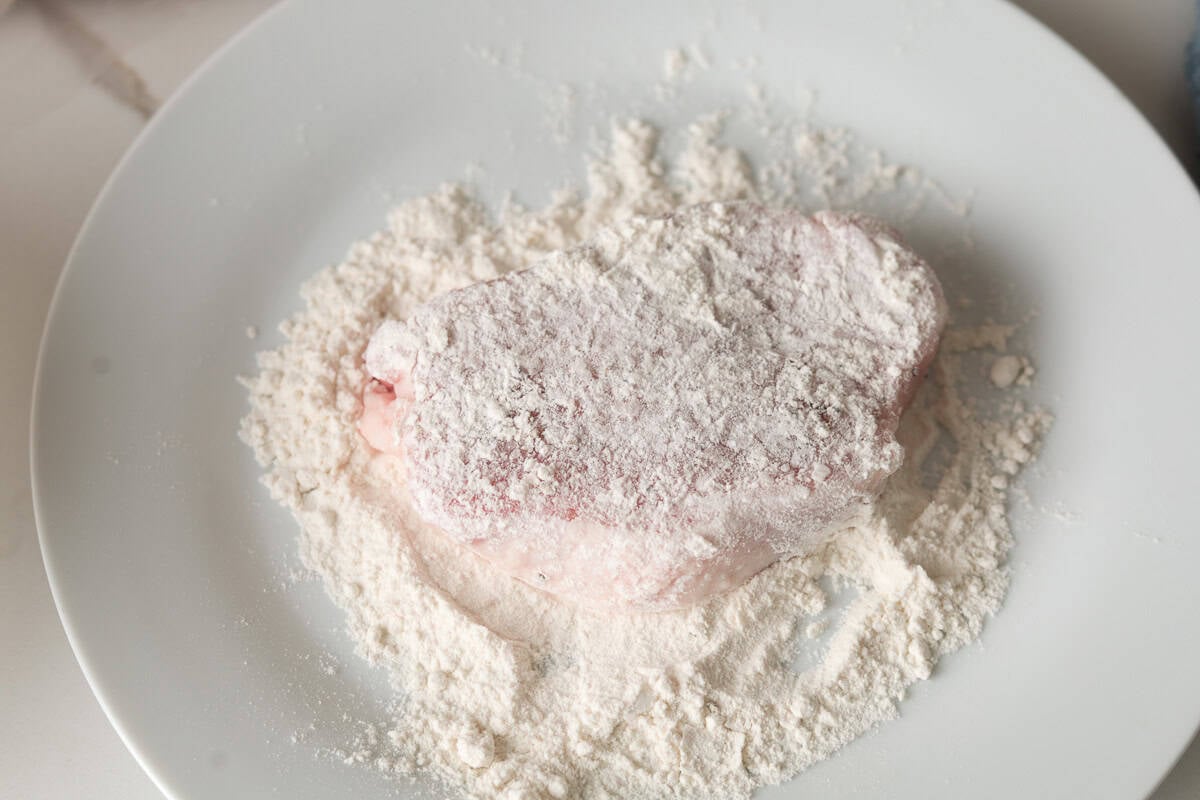 pork cutlet coated with flour on plate.