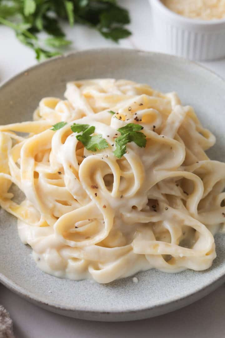 Plate of freshly tossed fettuccine Alfredo pasta, garnished with parsley and pepper.