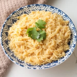 Overhead view of cooked orzo pasta garnished with fresh cilantro in a blue patterned porcelain bowl next to a dishcloth.