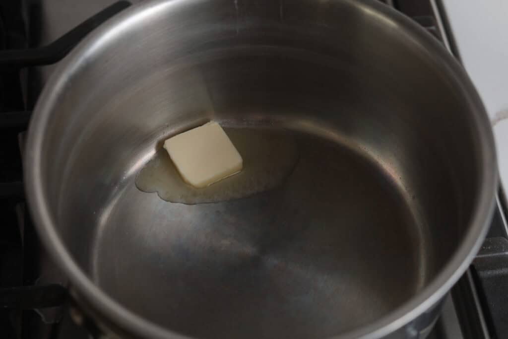 A square slice of butter melting at the bottom of a stainless steel saucepan.