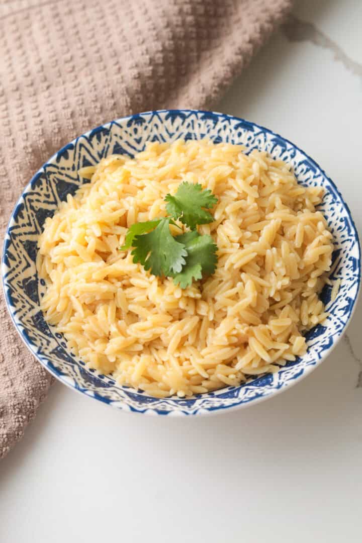 Vertical shot of cooked orzo garnished with cilantro in a blue-and-white decorative bowl.