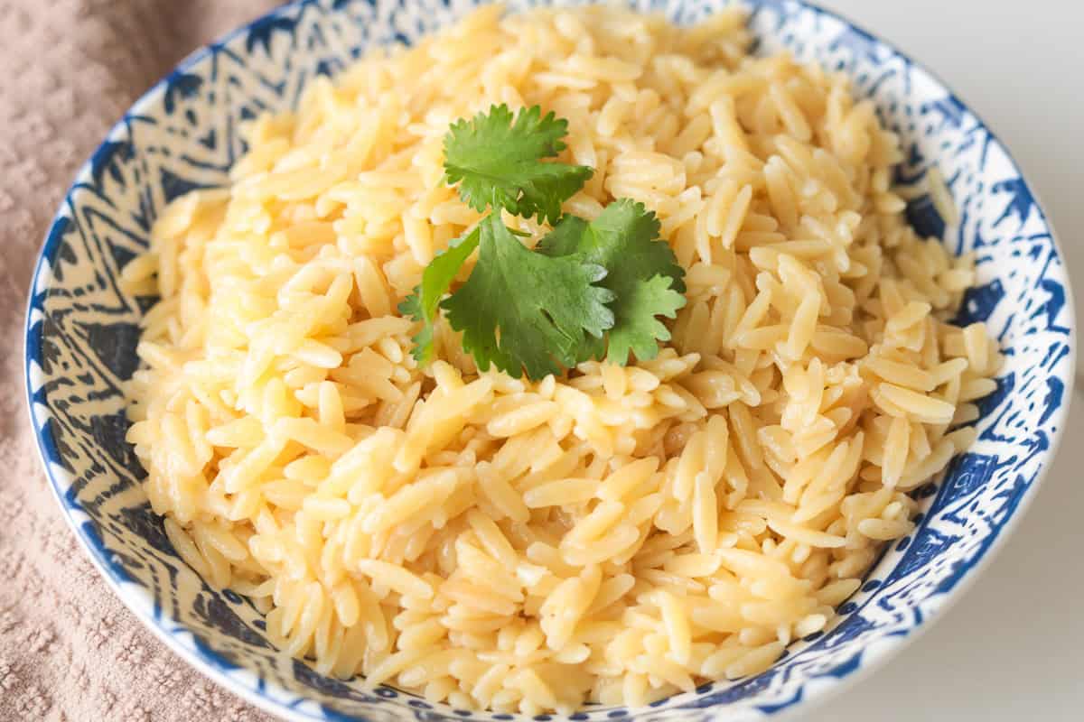 Close-up shot of creamy cooked orzo pasta topped with fresh green cilantro in a patterned bowl.