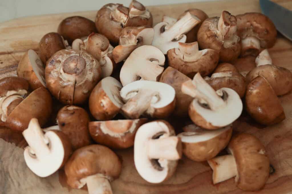 A pile of freshly chopped raw brown mushrooms resting on a wooden cutting board.