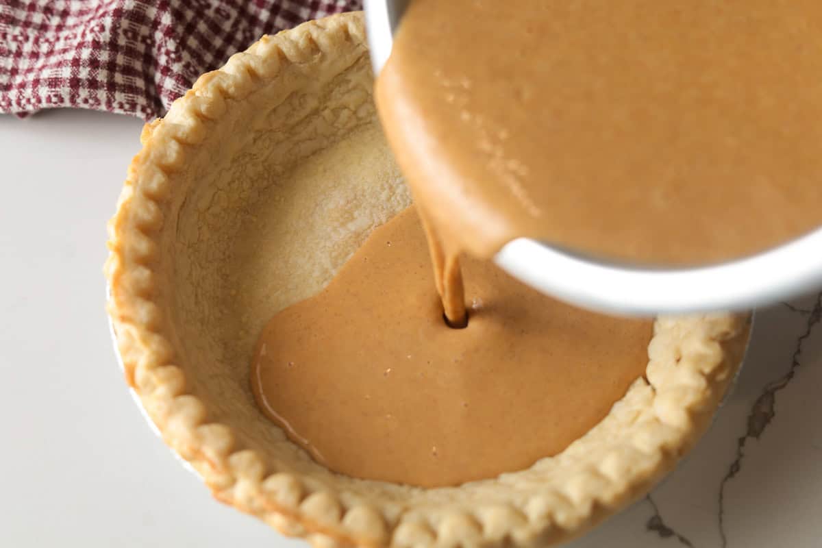 Pouring smooth pumpkin pie mixture into a unbaked pie shell.