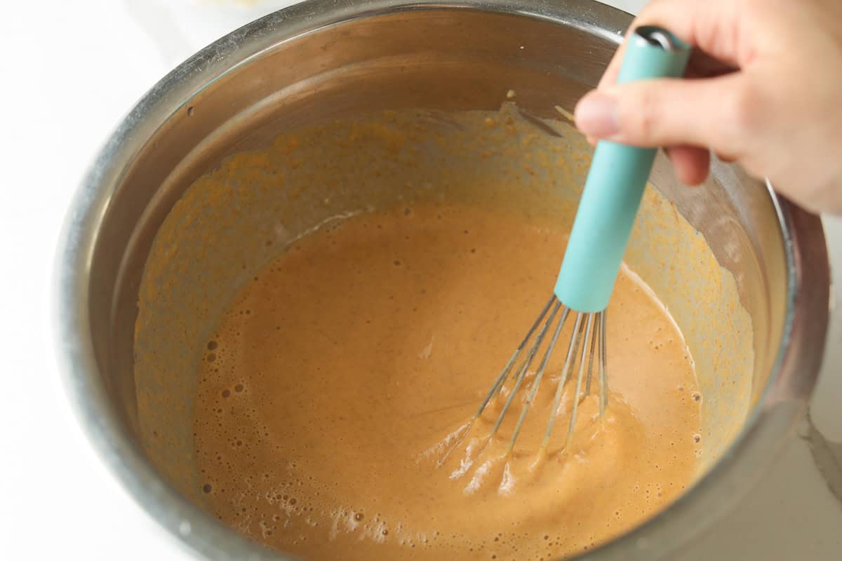 Whisking smooth pumpkin pie filling in a metal mixing bowl.