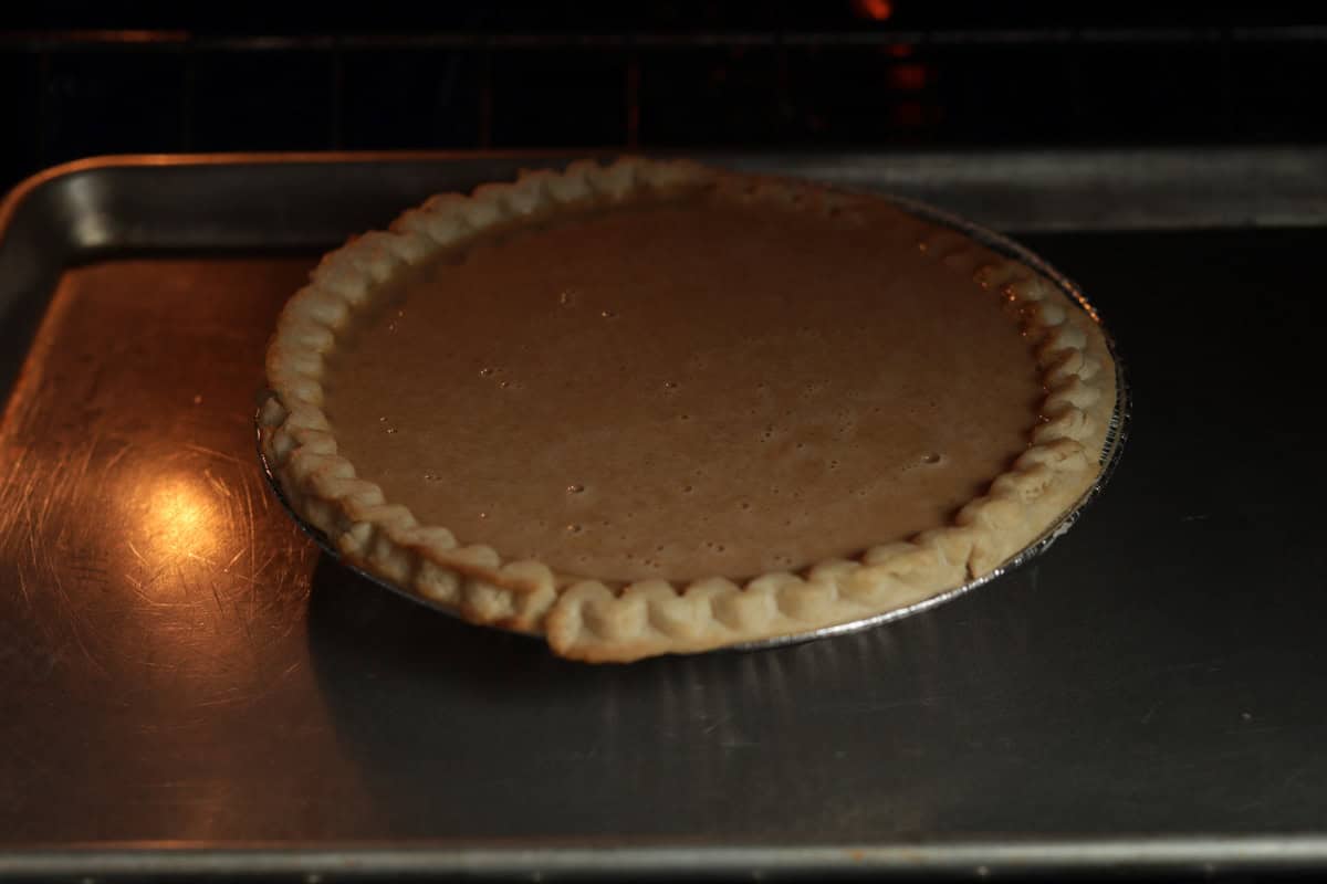 An unbaked pumpkin pie sitting on a baking sheet inside an oven.