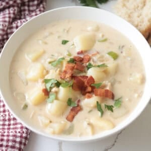 Bowl of clam chowder with diced potatoes and bacon topping on a marble surface.