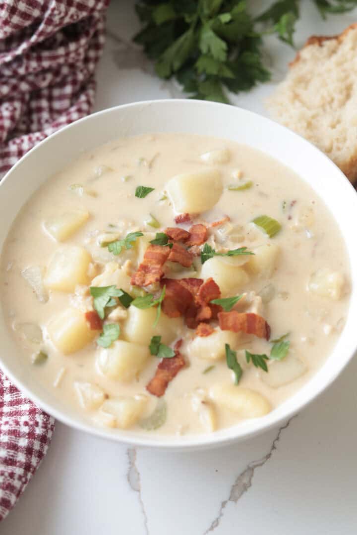 Vertical shot of clam chowder garnished with bacon bits and parsley, served alongside sliced bread.