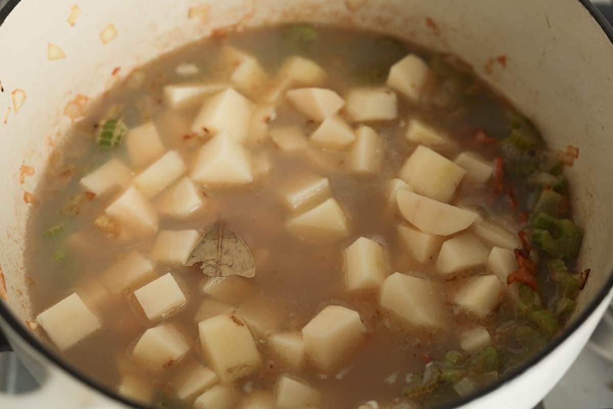 Diced potatoes and a bay leaf simmering in broth.